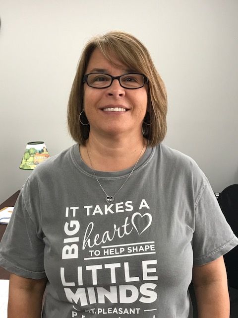A woman wearing a t-shirt that says `` it takes a big heart to help shape little minds '' is smiling.