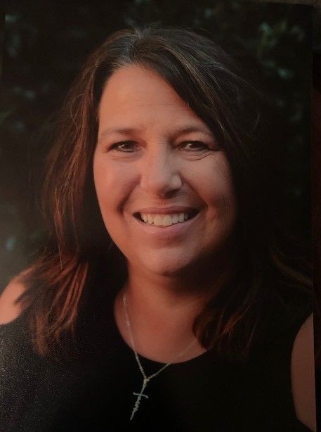 A woman is smiling and wearing a cross necklace.