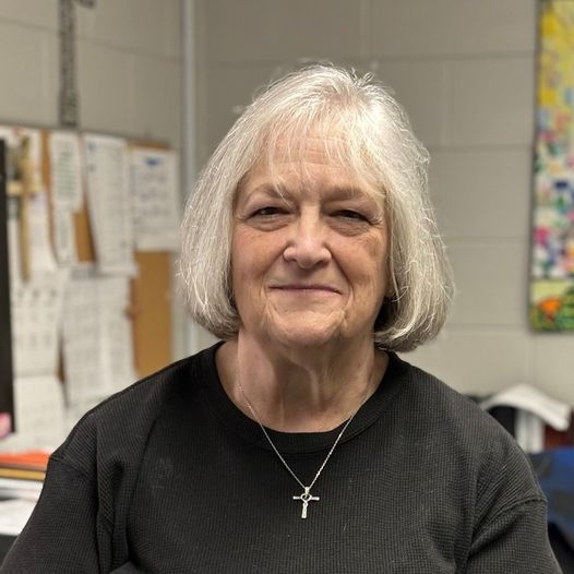 A woman wearing a black shirt and a cross necklace is smiling for the camera.