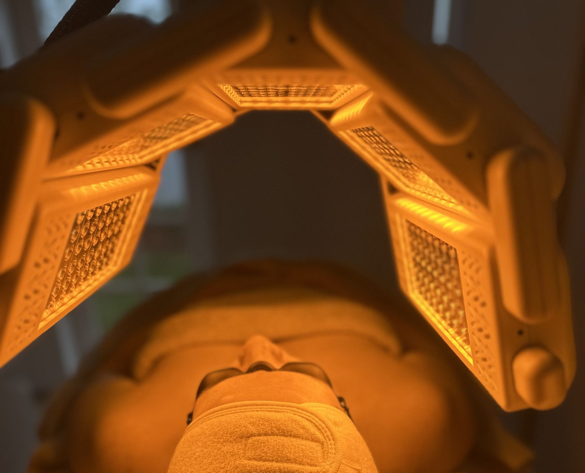 Person's face under orange LED light therapy device, receiving treatment in a clinical setting.— Bombshell Body Bar In Meikleville Hill, QLD