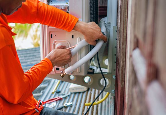 A man in an orange shirt is working on an air conditioner.