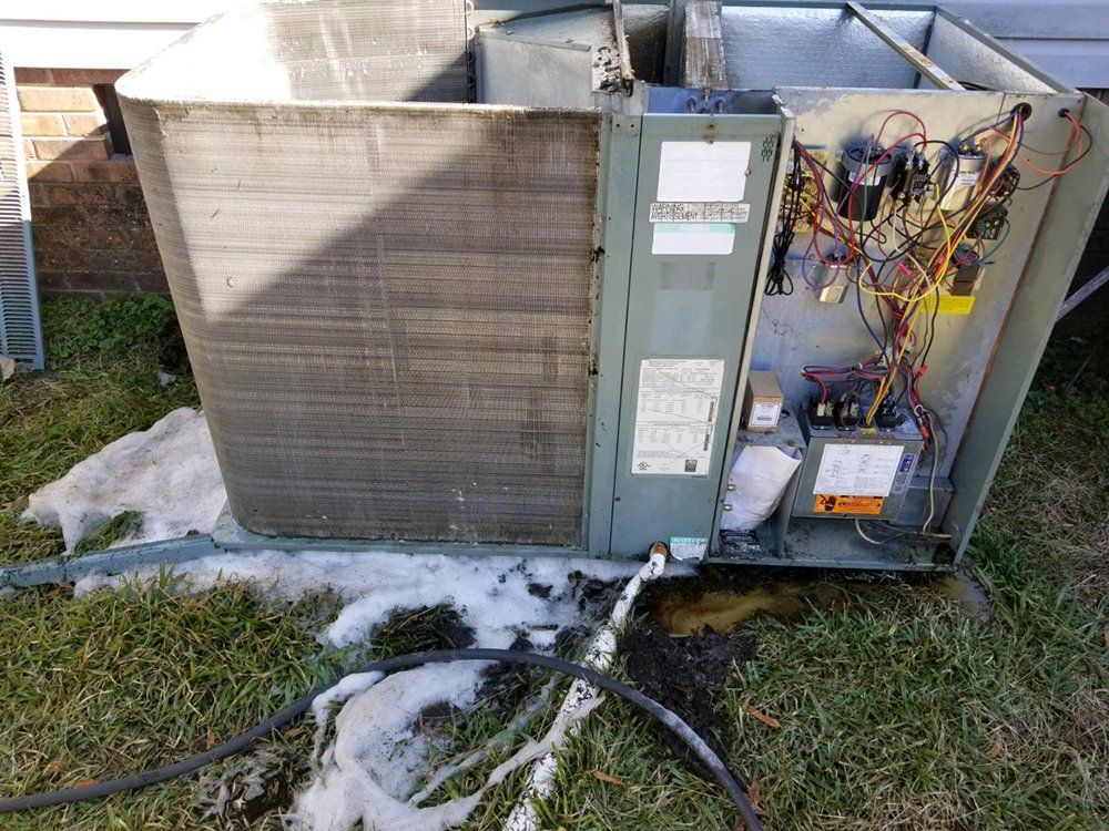 A broken air conditioner is sitting in the grass next to a house.