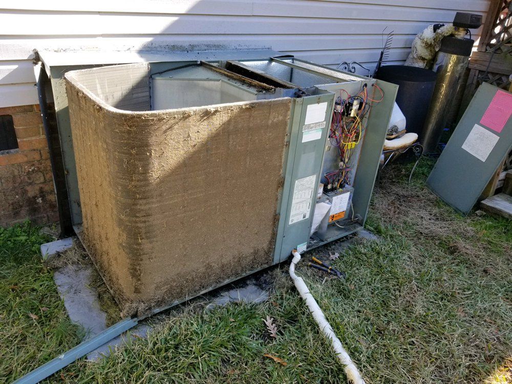 A dirty air conditioner is sitting in the grass next to a house.
