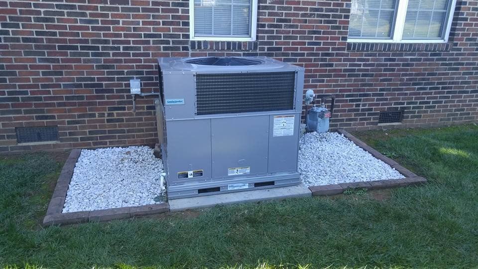 A large air conditioner is sitting in the grass in front of a brick building.