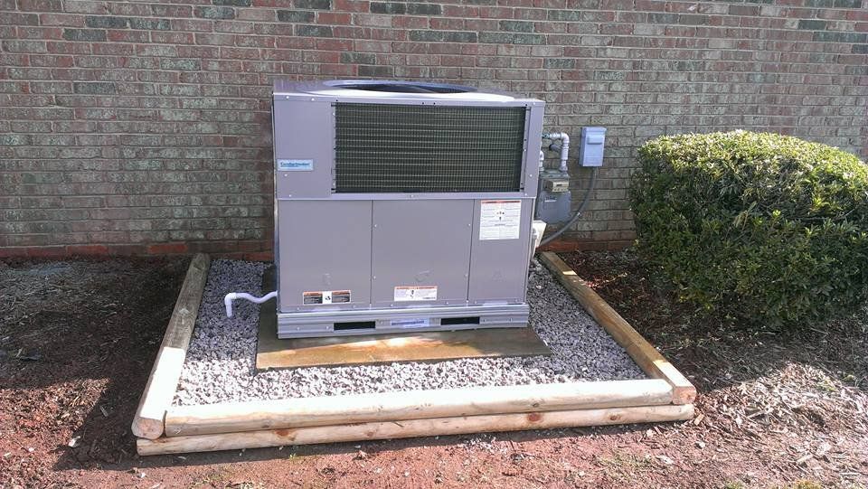 A large air conditioner is sitting on top of a pile of gravel in front of a brick building.