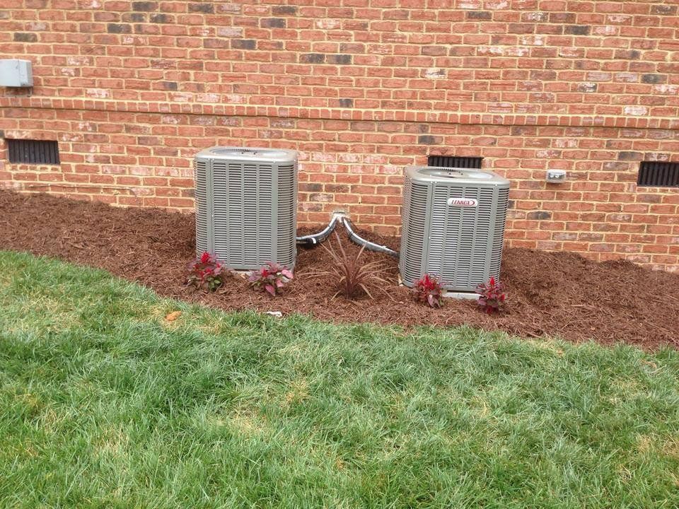 Two air conditioners are sitting next to each other on the side of a brick building.