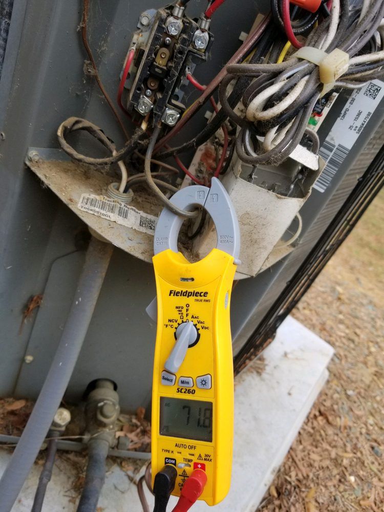 A yellow clamp meter is being used to measure the voltage of an air conditioner.