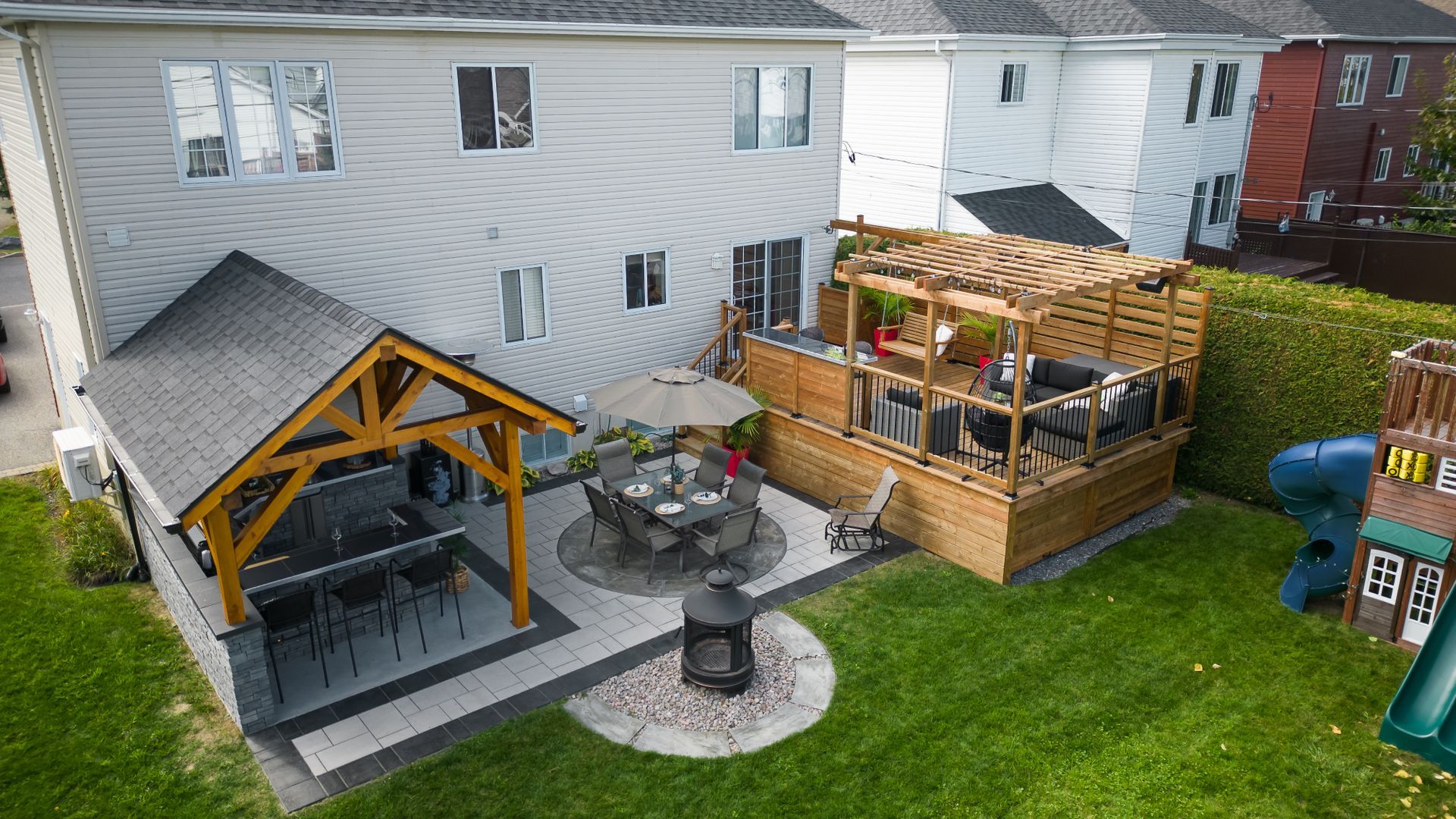 Une vue aérienne d'une cour arrière avec une pergola, une table, des chaises et un toboggan.