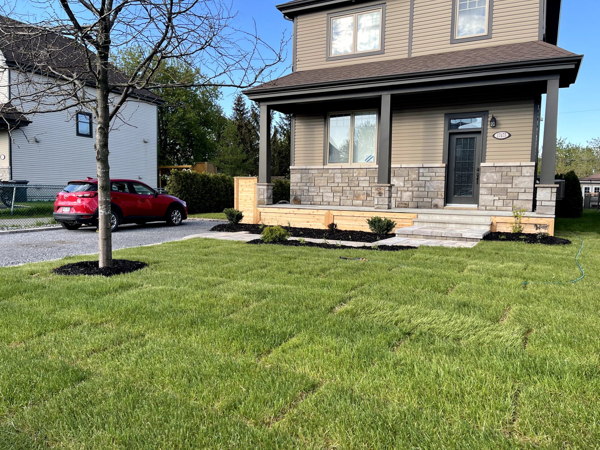 Une voiture rouge est garée devant une maison avec une pelouse verte luxuriante.