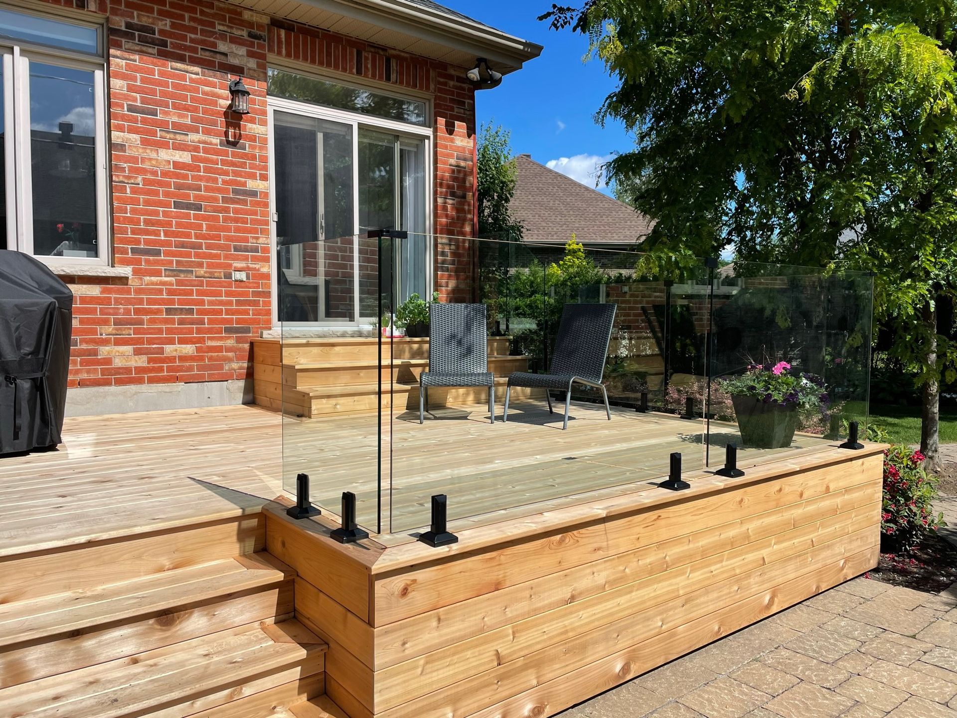 Une terrasse en bois avec une balustrade en verre devant une maison en brique.