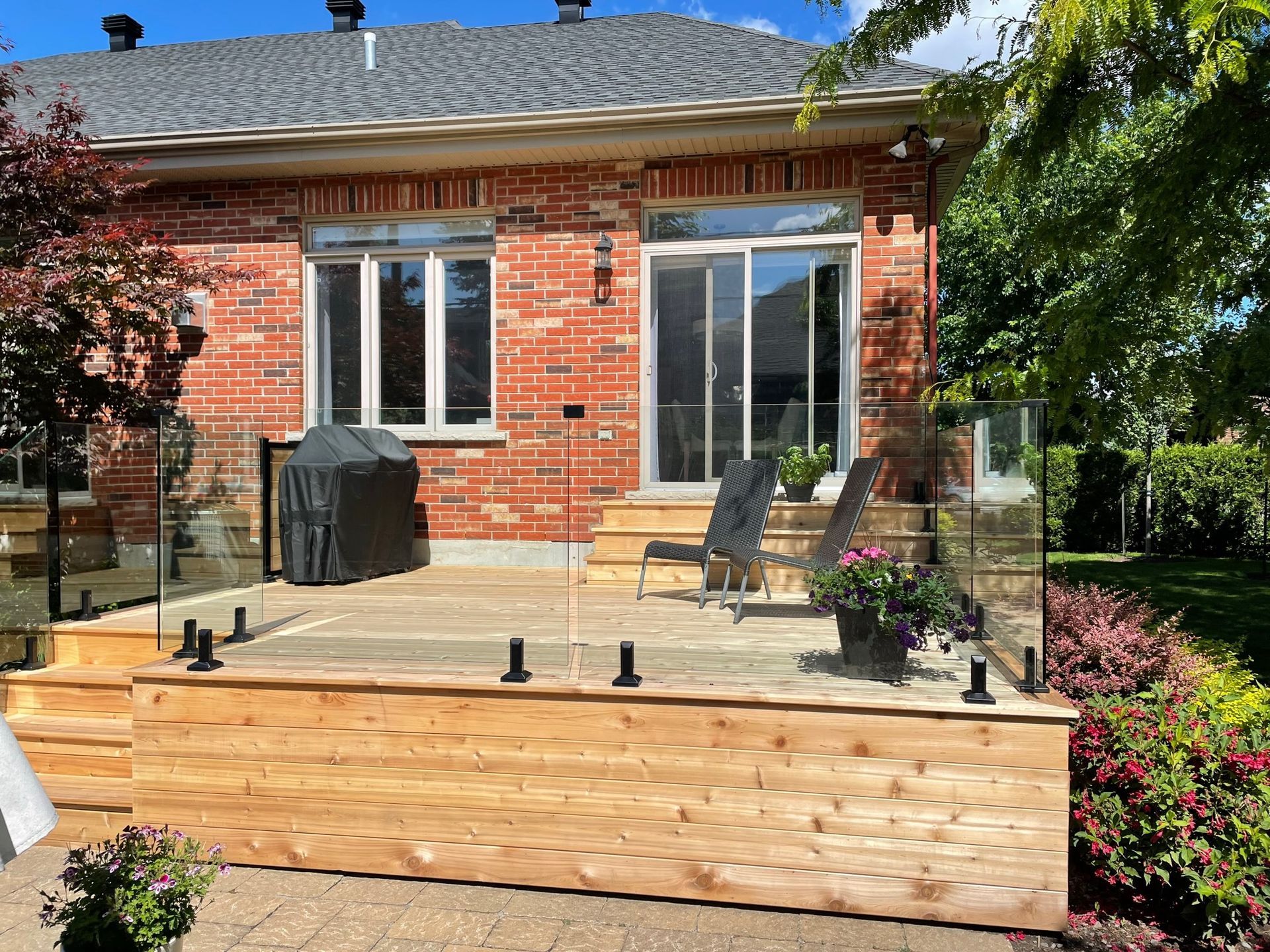 Une maison en briques avec une terrasse en bois et une balustrade en verre.