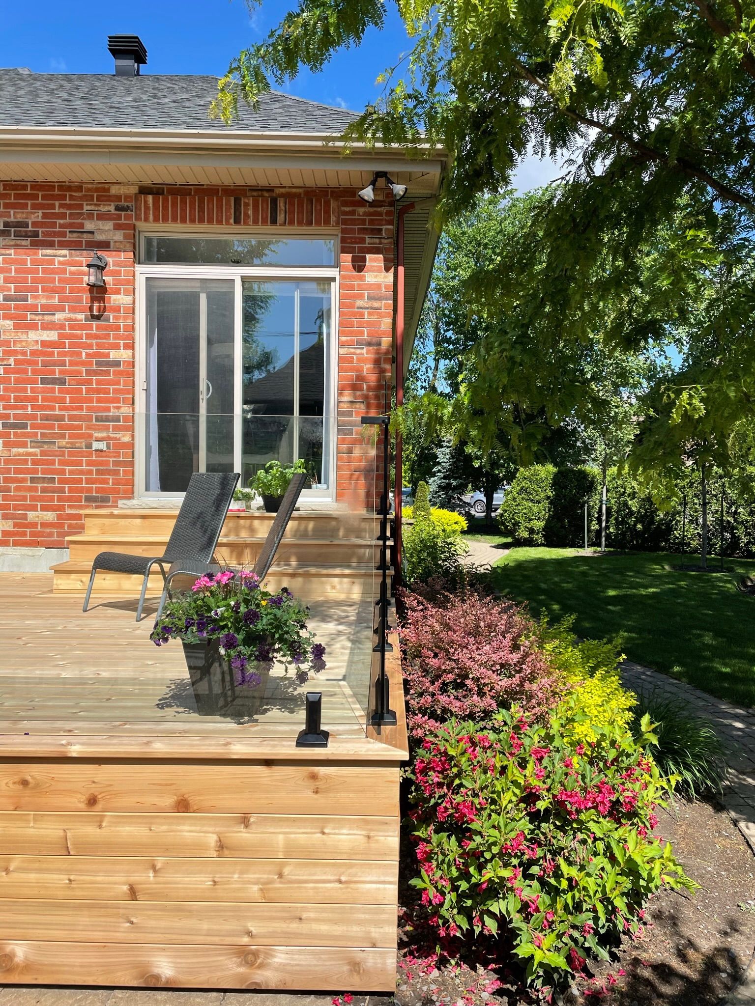 Terrasse en bois à côté d'une maison en briques avec porte coulissante en verre. Parterre de fleurs aux couleurs vives.