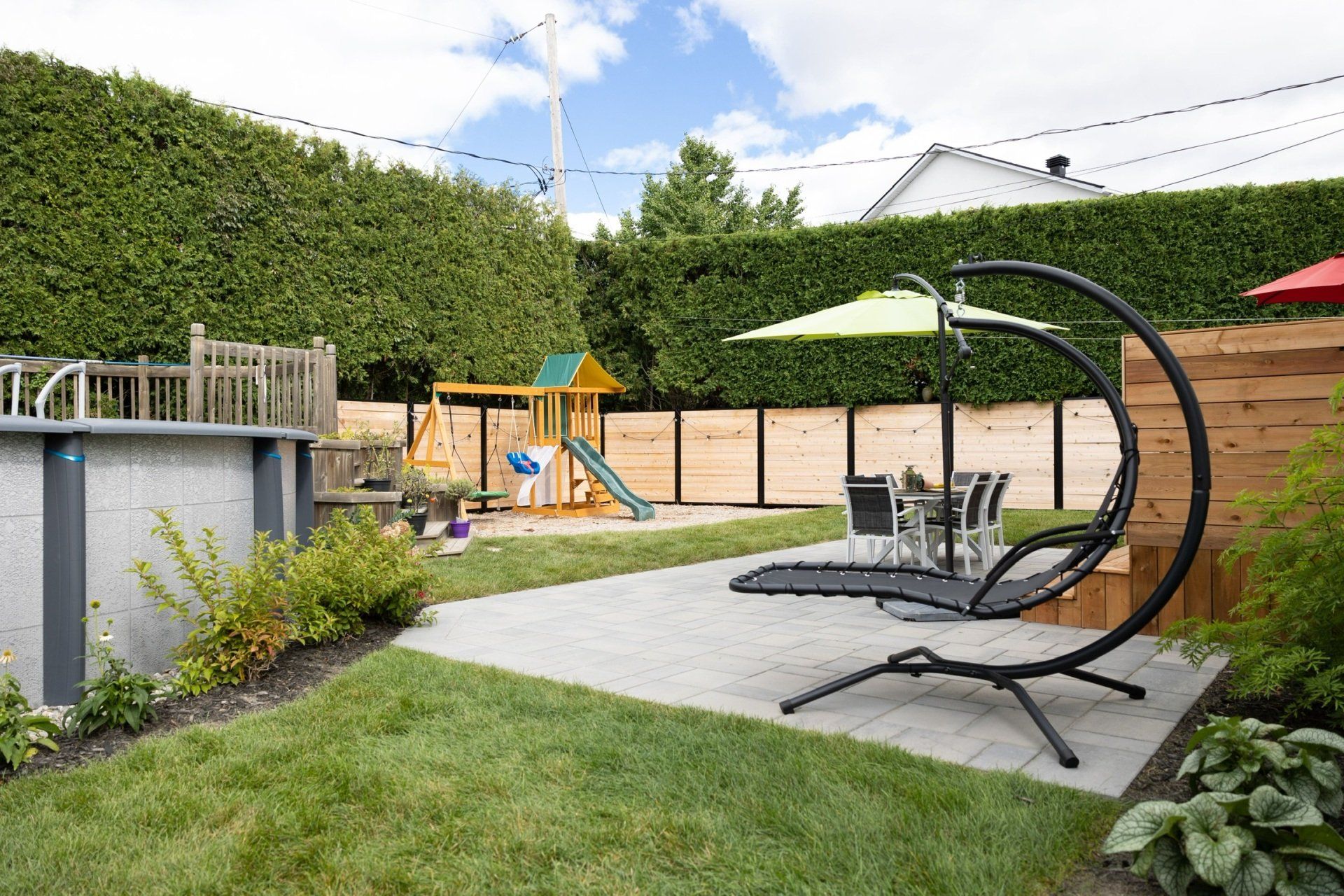 Une cour arrière avec piscine, balançoires, chaises, parasols et une aire de jeux.