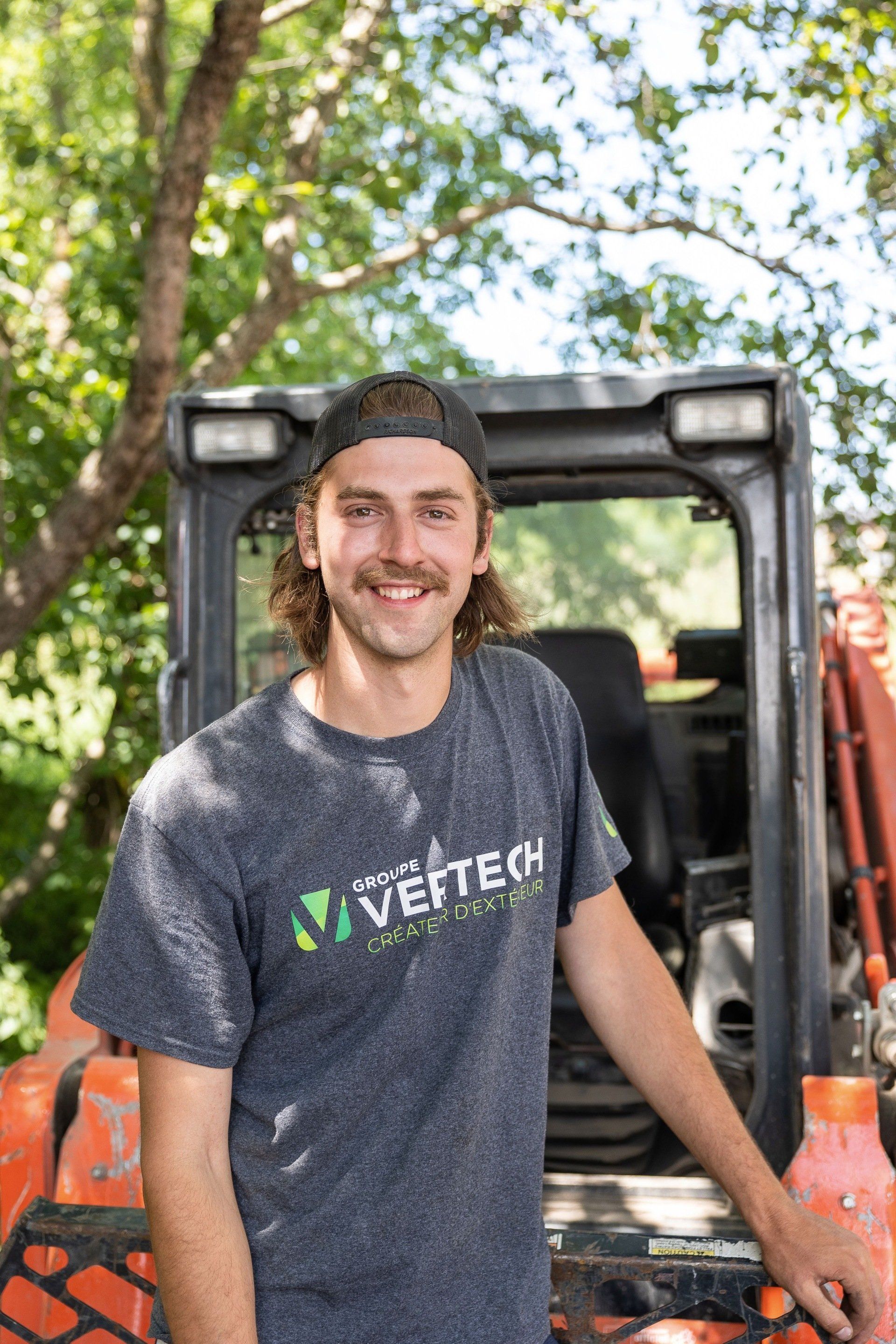 Un jeune homme se tient devant un bulldozer.
