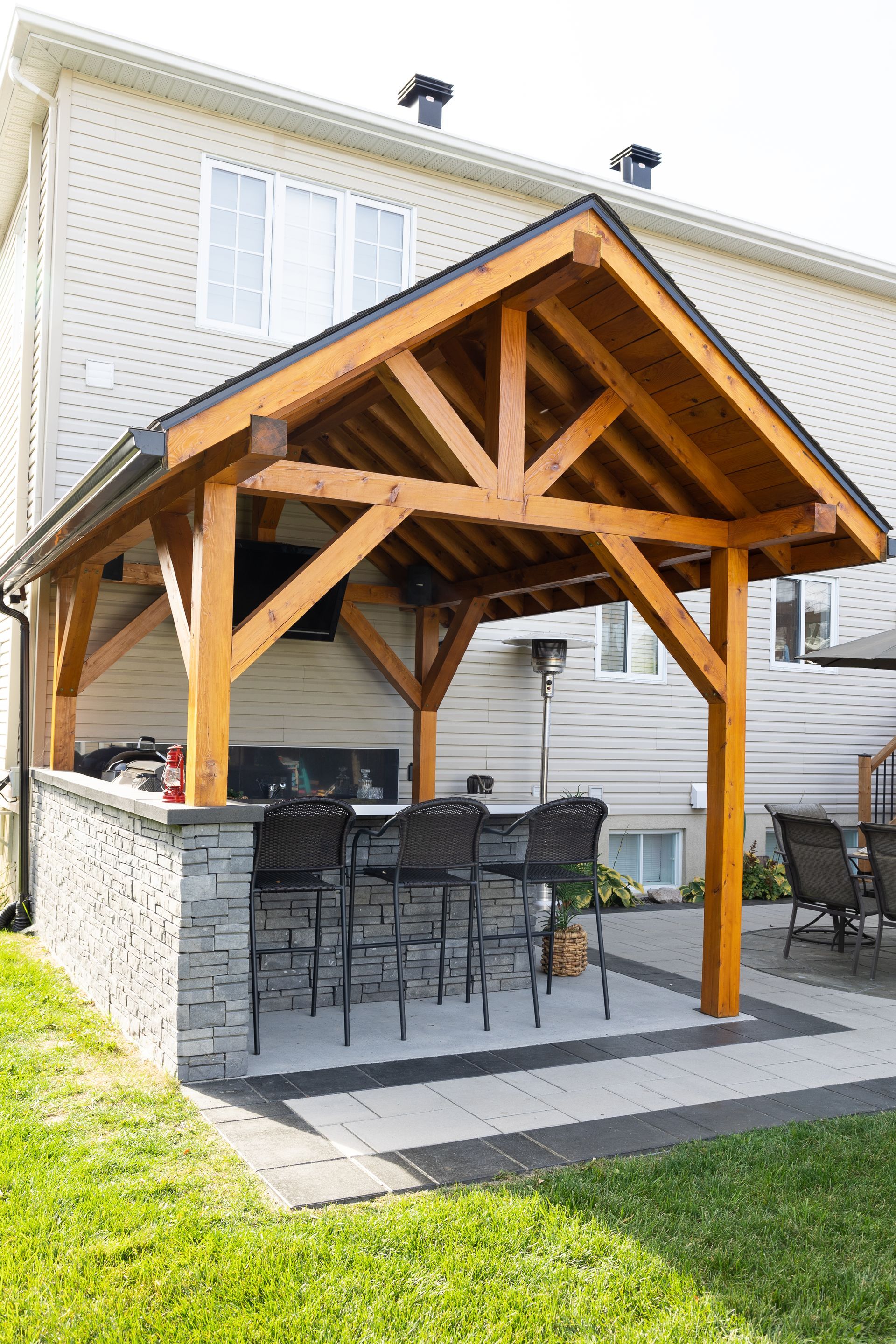Un gazebo en bois avec une table et des chaises en dessous devant une maison.