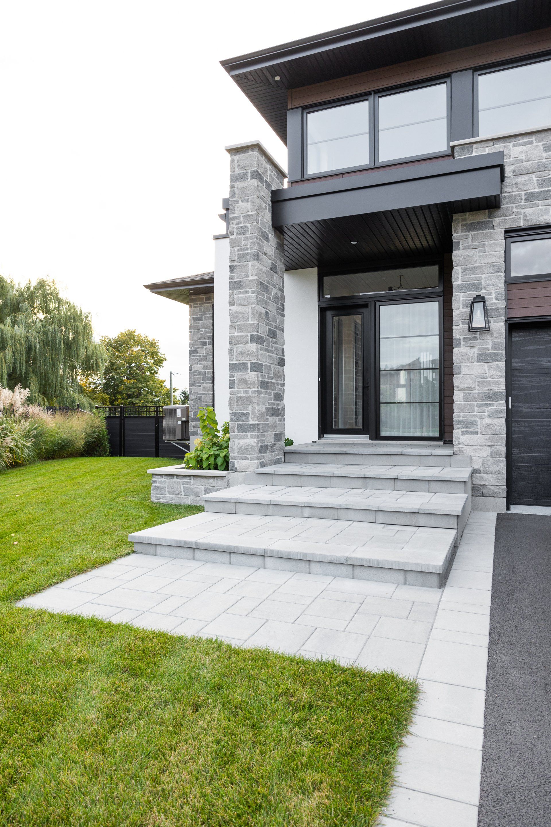 Une maison moderne avec des escaliers menant à la porte d'entrée et une porte de garage noire.