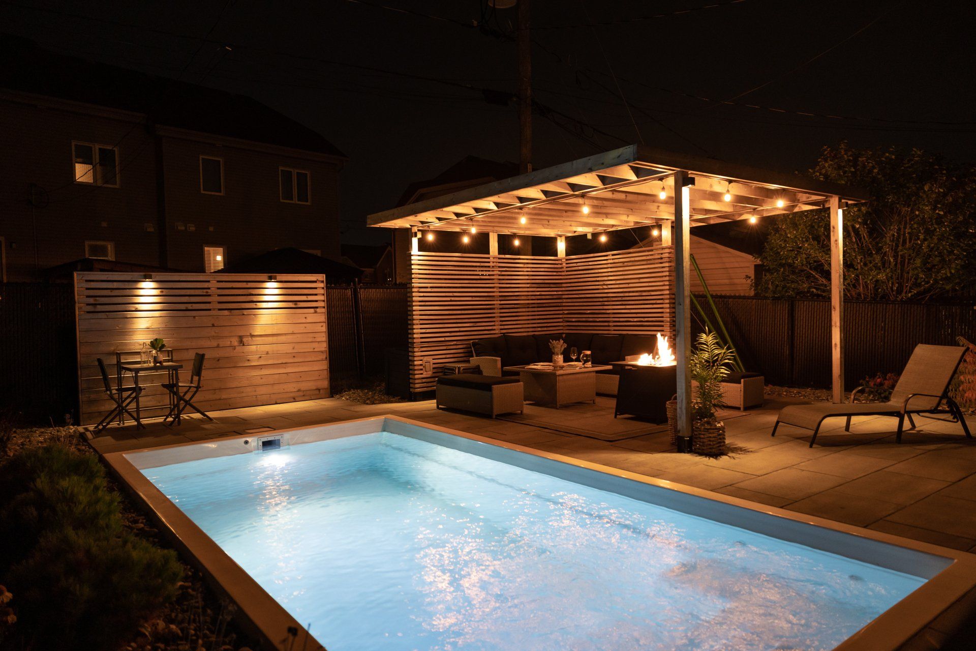 Une grande piscine est éclairée la nuit dans une cour arrière.