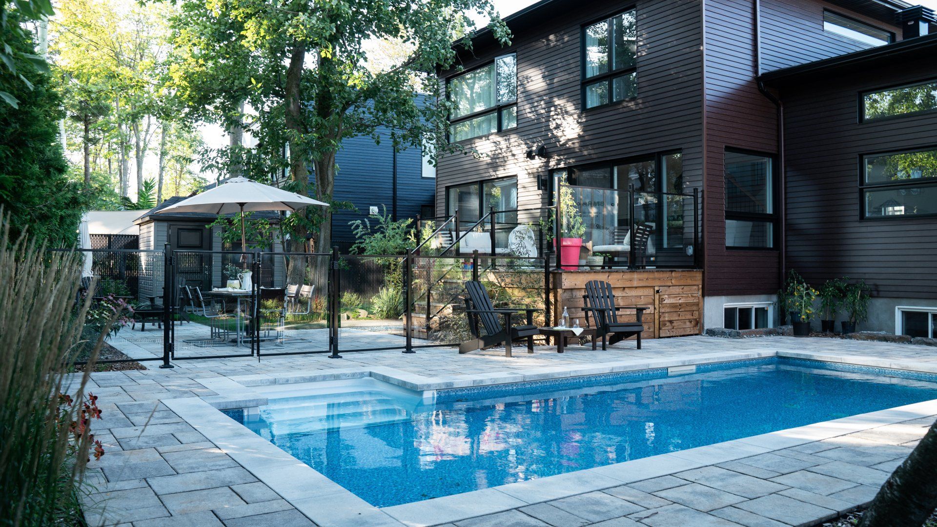 Jardin avec piscine, terrasse et maison moderne à deux étages avec revêtement extérieur foncé.