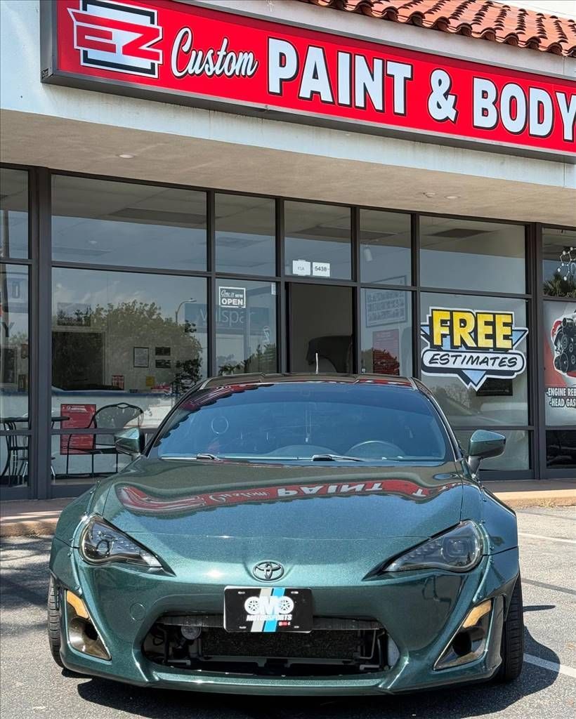Green Toyota sports car parked in front of a custom paint and body shop.