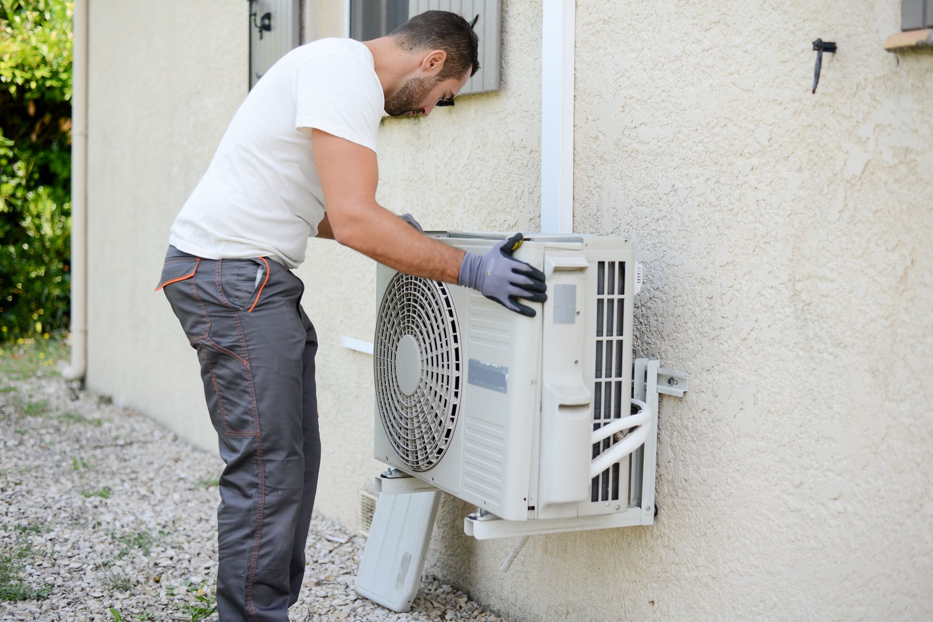 Un homme en vêtements de travail installe une unité de climatisation à l'extérieur d'un bâtiment.