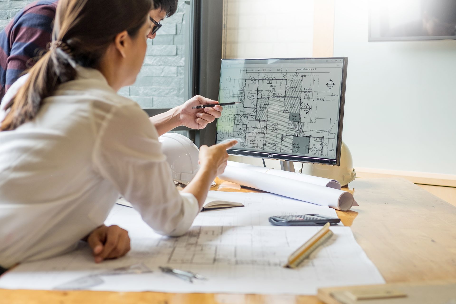 Personne examinant des plans architecturaux à un bureau avec un ordinateur portable et des plans roulés