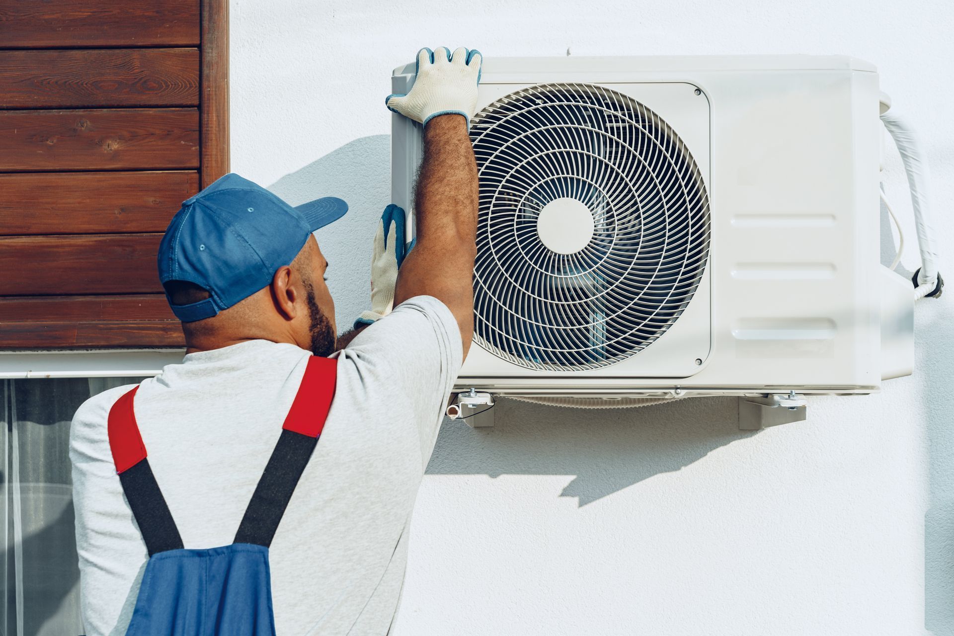 Un homme installe un climatiseur sur le côté d'un bâtiment.
