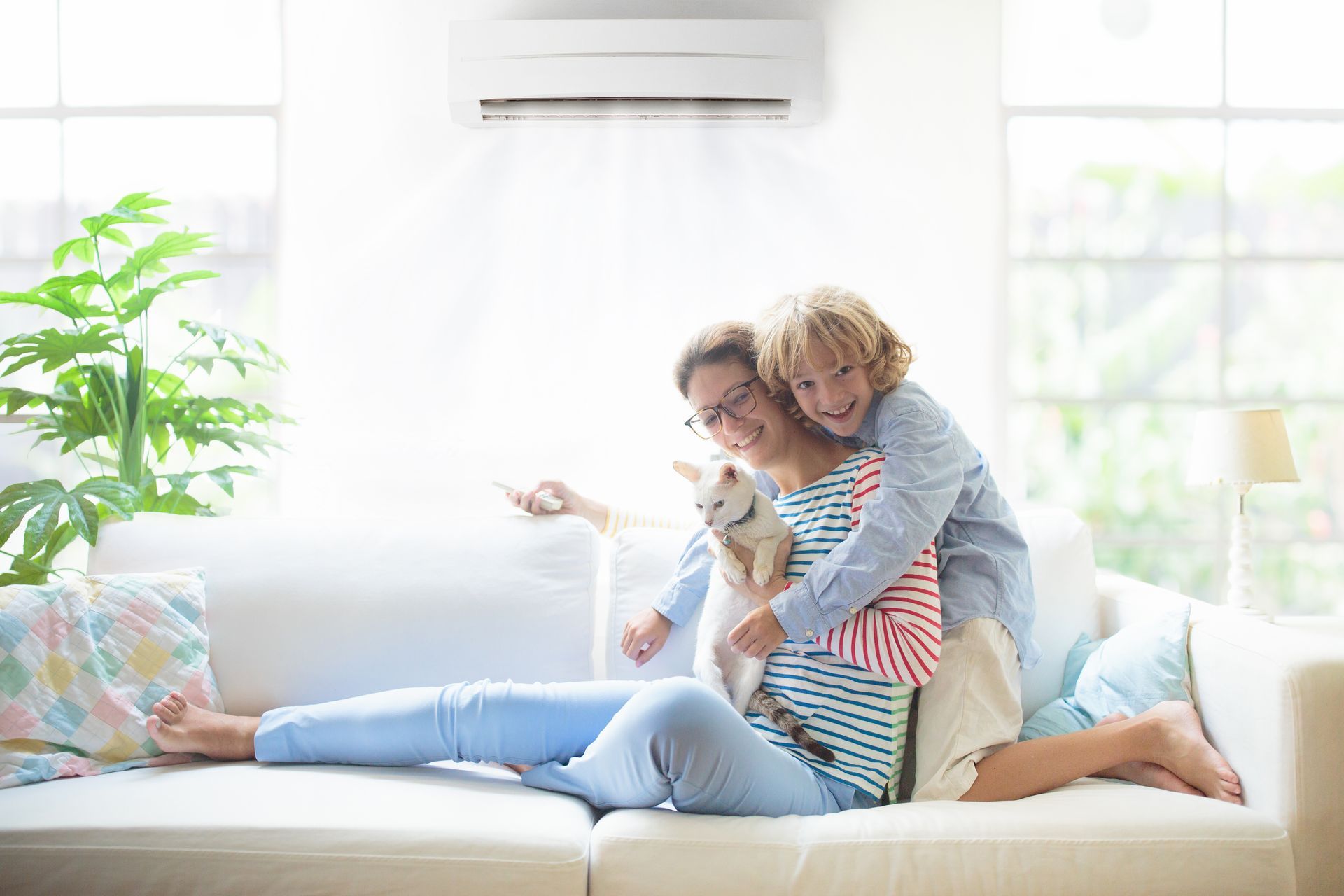 Femme, enfant et chat sur un canapé climatisé. La mère sourit, l'enfant la serre dans ses bras, le chat est assis dans ses bras. À l'intérieur.