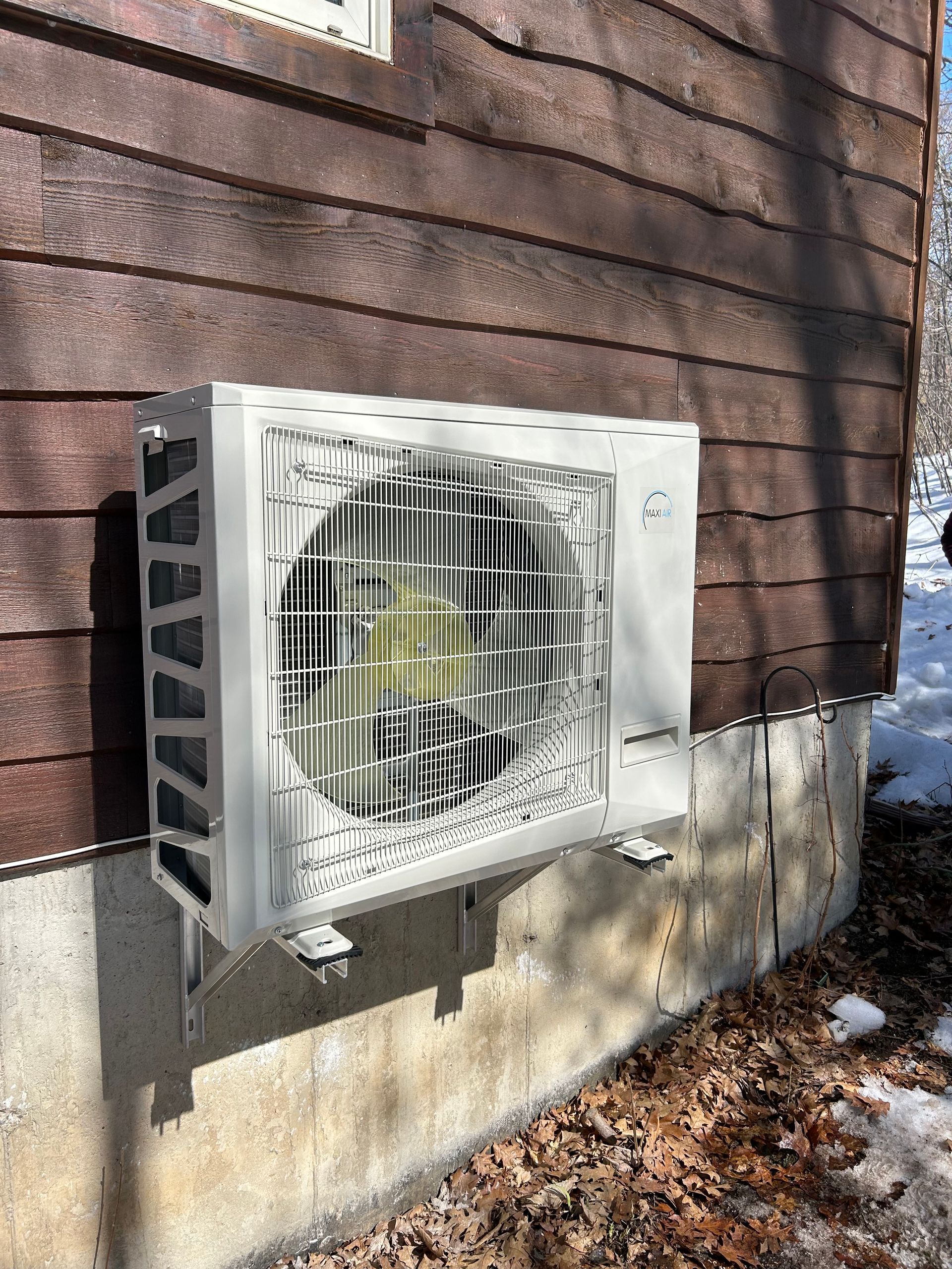 Un climatiseur blanc est monté sur le côté d’une maison en bois.