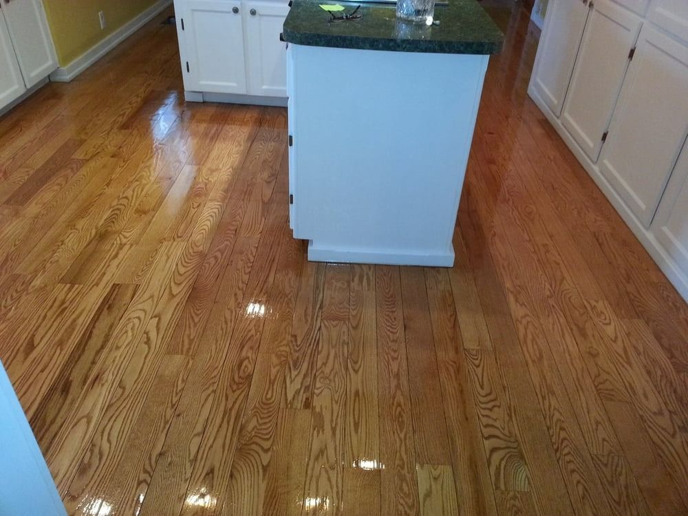 Hardwood kitchen floor with shiny finish, surrounding white cabinets and island with dark countertop.