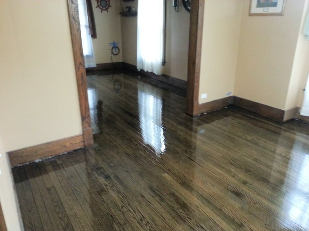 Refinished hardwood floor, dark stain, glossy finish reflecting light in a room with beige walls and dark wood trim.