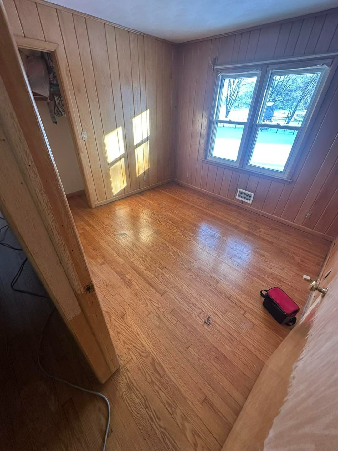 Empty room with wood paneling, hardwood floor, window, and small closet.