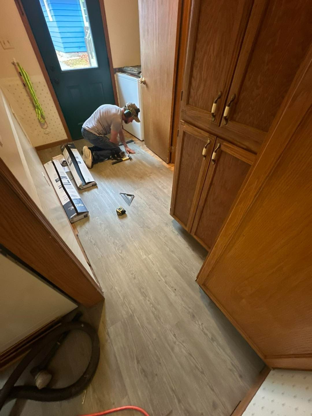 Person installing flooring in a room with wood cabinets and a door, tools and planks visible.
