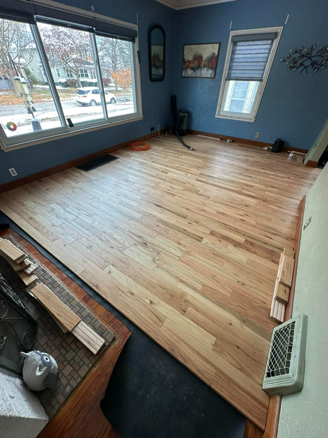 Hardwood flooring being installed in a room with blue walls, a large window, and scattered tools.
