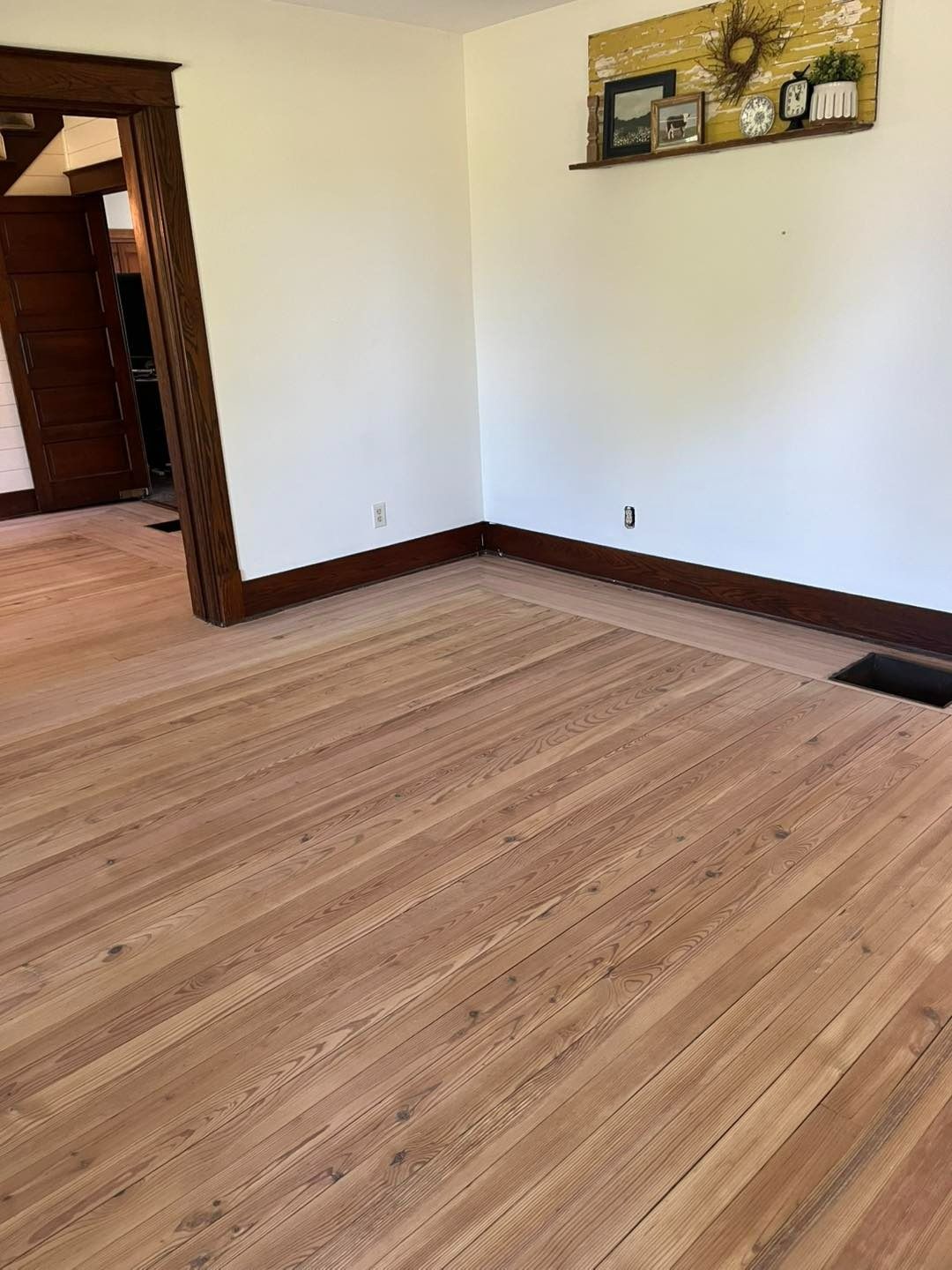 Wooden floors and white walls in an empty room, dark wood trim around a doorway.