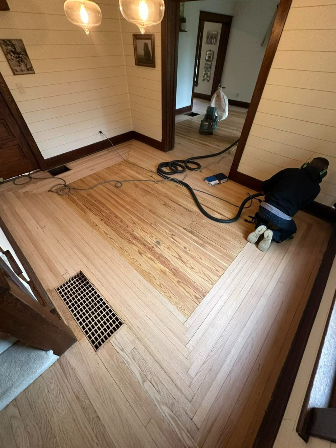 Person kneeling, vacuuming a hardwood floor with a central patterned section.