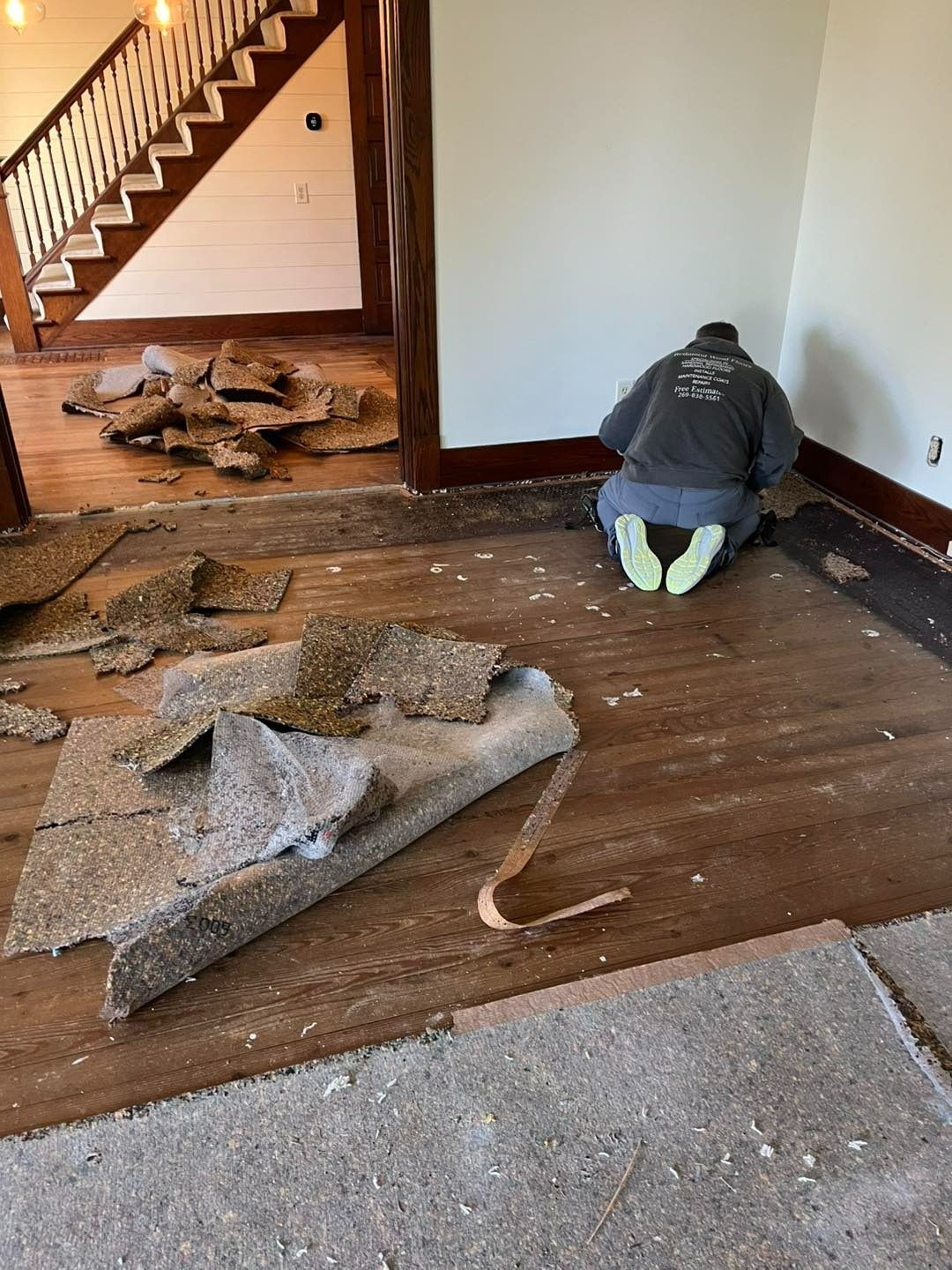 Person removing carpet in a room with hardwood floors, a staircase, and white walls.