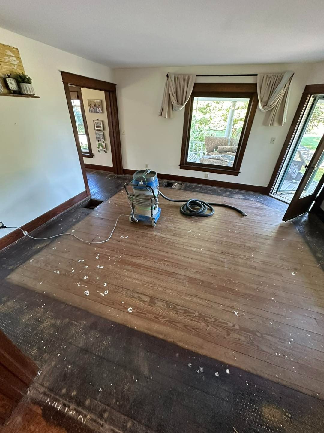 Wooden floor being sanded with a machine; interior room with windows and open doorways.