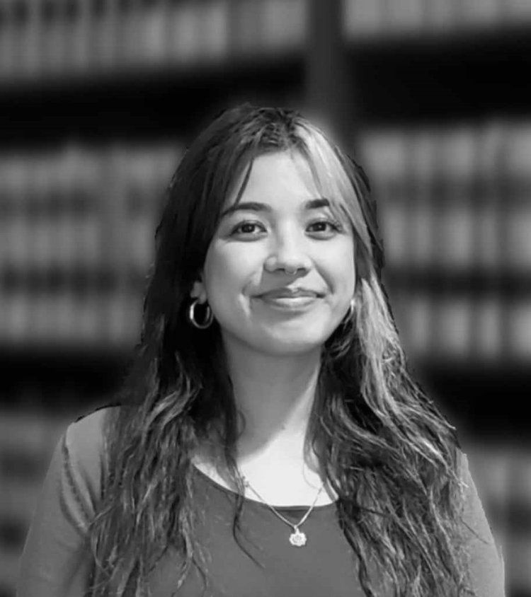 A black and white photo of a woman smiling in front of a bookshelf.