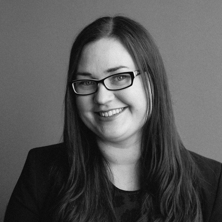 a woman wearing glasses and a black jacket smiles in a black and white photo