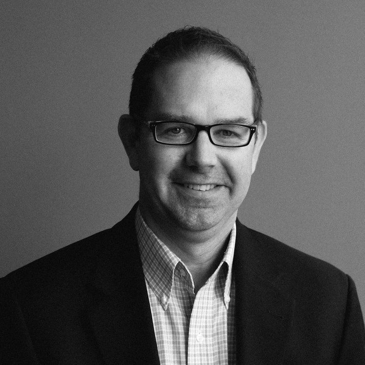 a man wearing glasses and a suit smiles for the camera