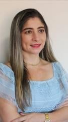 Uma mulher de blusa azul está de pé com os braços cruzados e sorrindo.