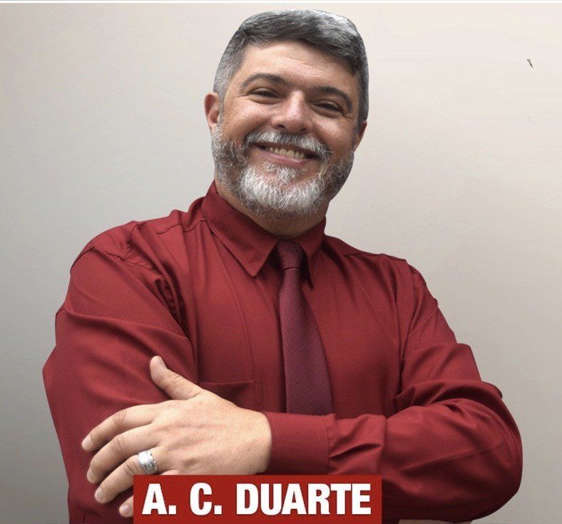 Um homem de camisa vermelha e gravata com o nome ac duarte
