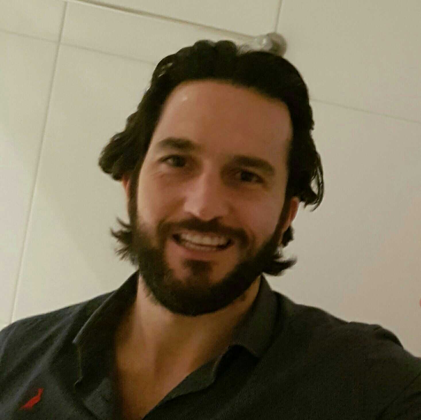 Um homem com barba e cabelo comprido está sorrindo para a câmera.