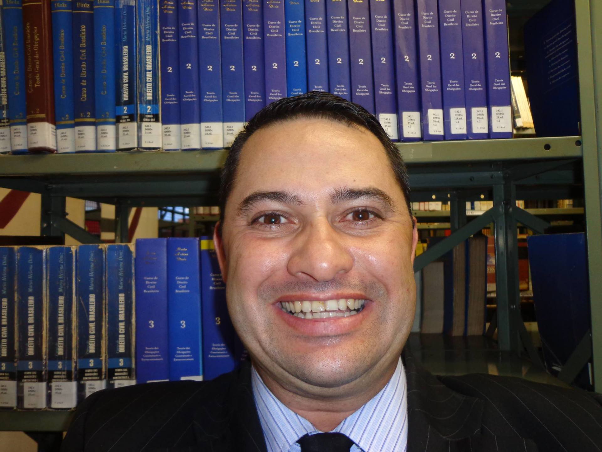 Um homem de terno e gravata está sorrindo em frente a uma estante cheia de livros