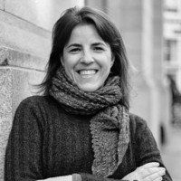 Uma mulher vestindo um lenço e um suéter está sorrindo em uma foto em preto e branco.