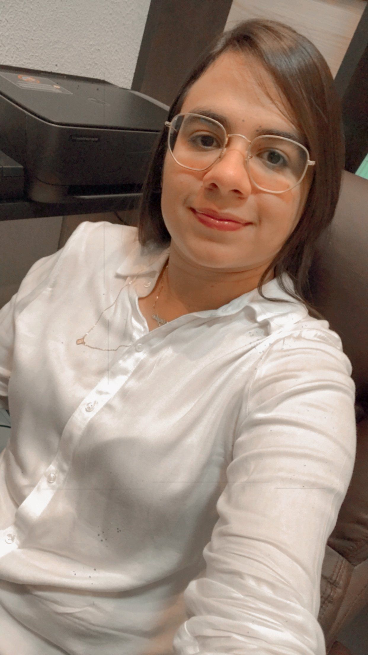 Uma mulher de óculos e camisa branca está tirando uma selfie.