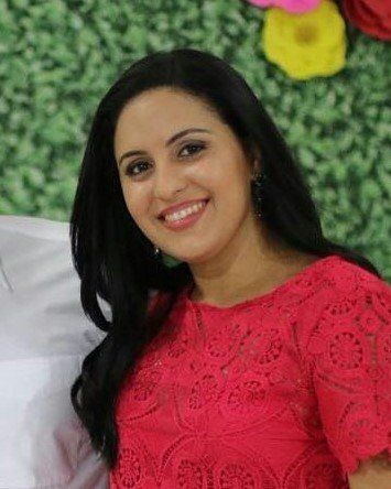 Uma mulher de blusa vermelha está sorrindo enquanto está deitada na cama.