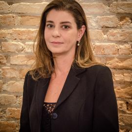 Uma mulher de jaqueta preta está parada em frente a uma parede de tijolos.