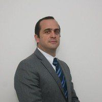 Um homem de terno e gravata está parado em frente a uma parede branca.