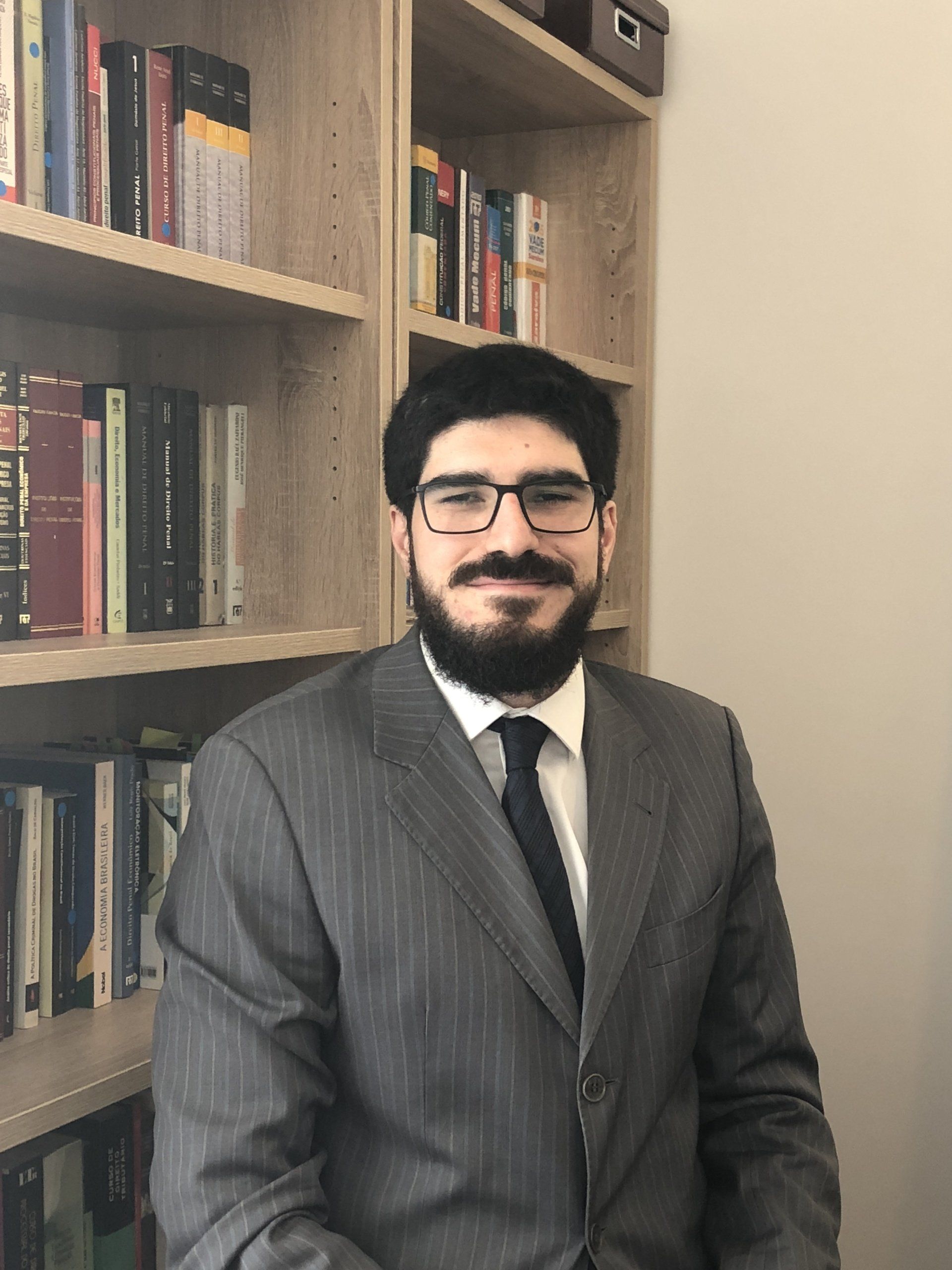 Um homem de terno e gravata está sentado em frente a uma estante.